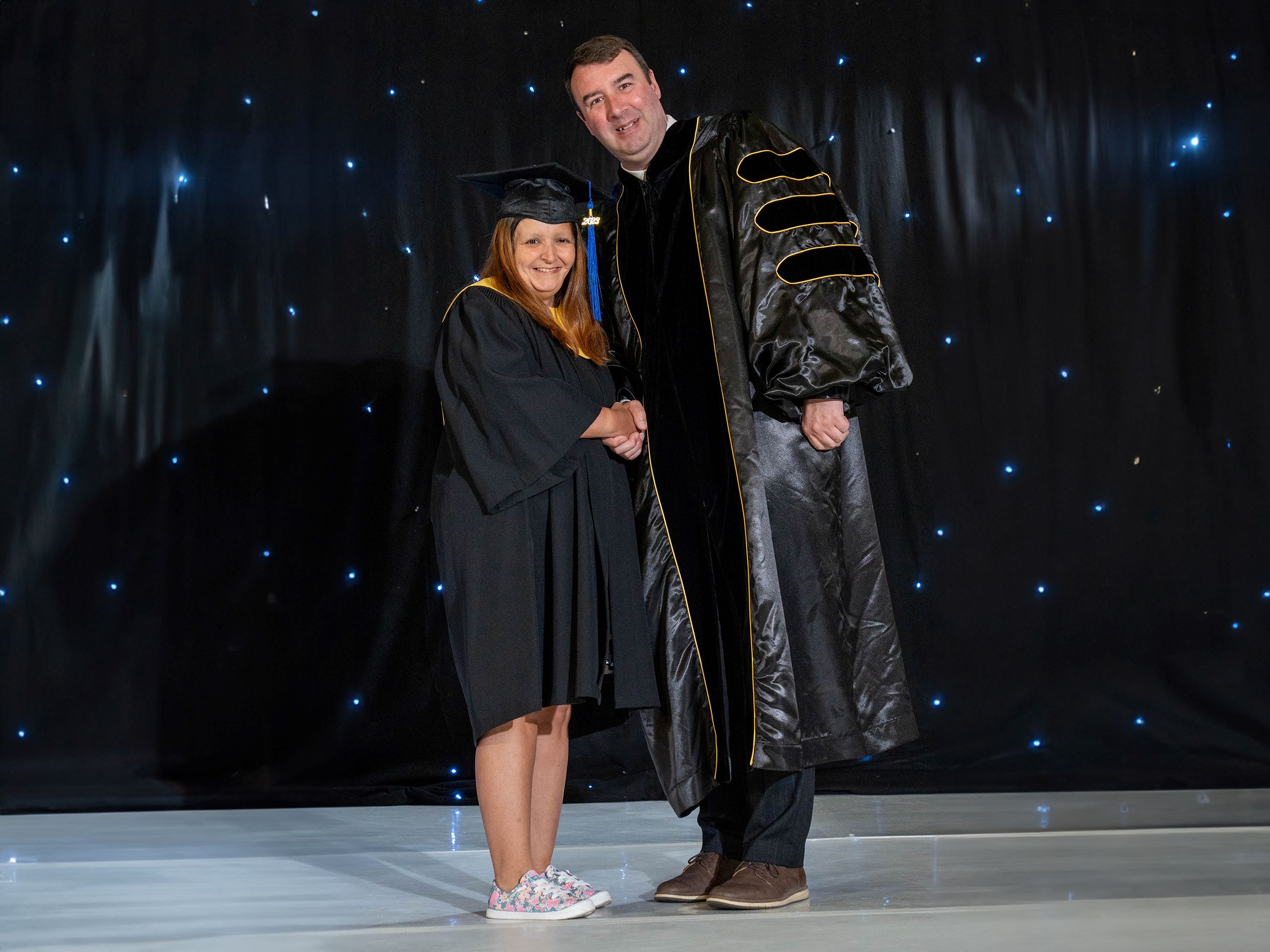 Valerie R., proud Sundance College Medical Office Admin graduate holds her graduation scroll in one hand and shakes hands with the other hand, as she is congratulated by the College President, Dean Olsen at the Calgary 2023 graduation ceremony.